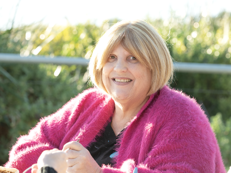 Woman smiling and wearing a pink sweater outside