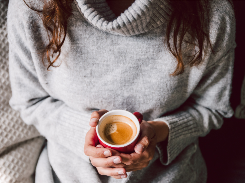 A woman in a sweater holding a coffee with two hands